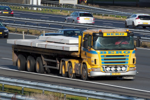 Ein gelber Sattelschlepper f√§hrt auf einer Autobahn neben anderen Autos, mit einer Person am Steuer, und einem Hintergrund mit Gel√§ndern, Gras, Texttafeln, Polen, B√§umen und Geb√§uden.