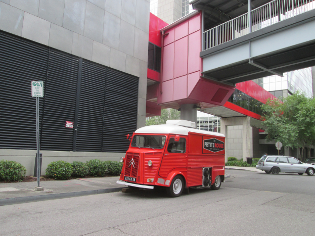 Ein Transporter ist in der Mitte des Bildes mit einem Auto auf der rechten Seite, und Gebäude sind im Hintergrund zu sehen.