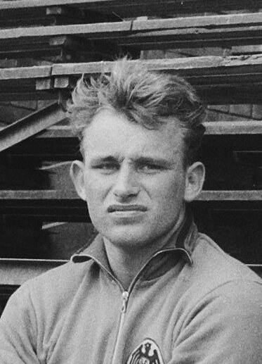 Schwarz-weißes Foto eines Mannes in einer Jacke vor gestapelten Holzplanken, der legendäre deutsche Fußballspieler soll es sein.