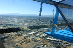 Luftaufnahme einer Stadt mit Häusern, Bäumen, einer Fußgängerbrücke auf der linken Seite, Hügel im Hintergrund und Himmel darüber.