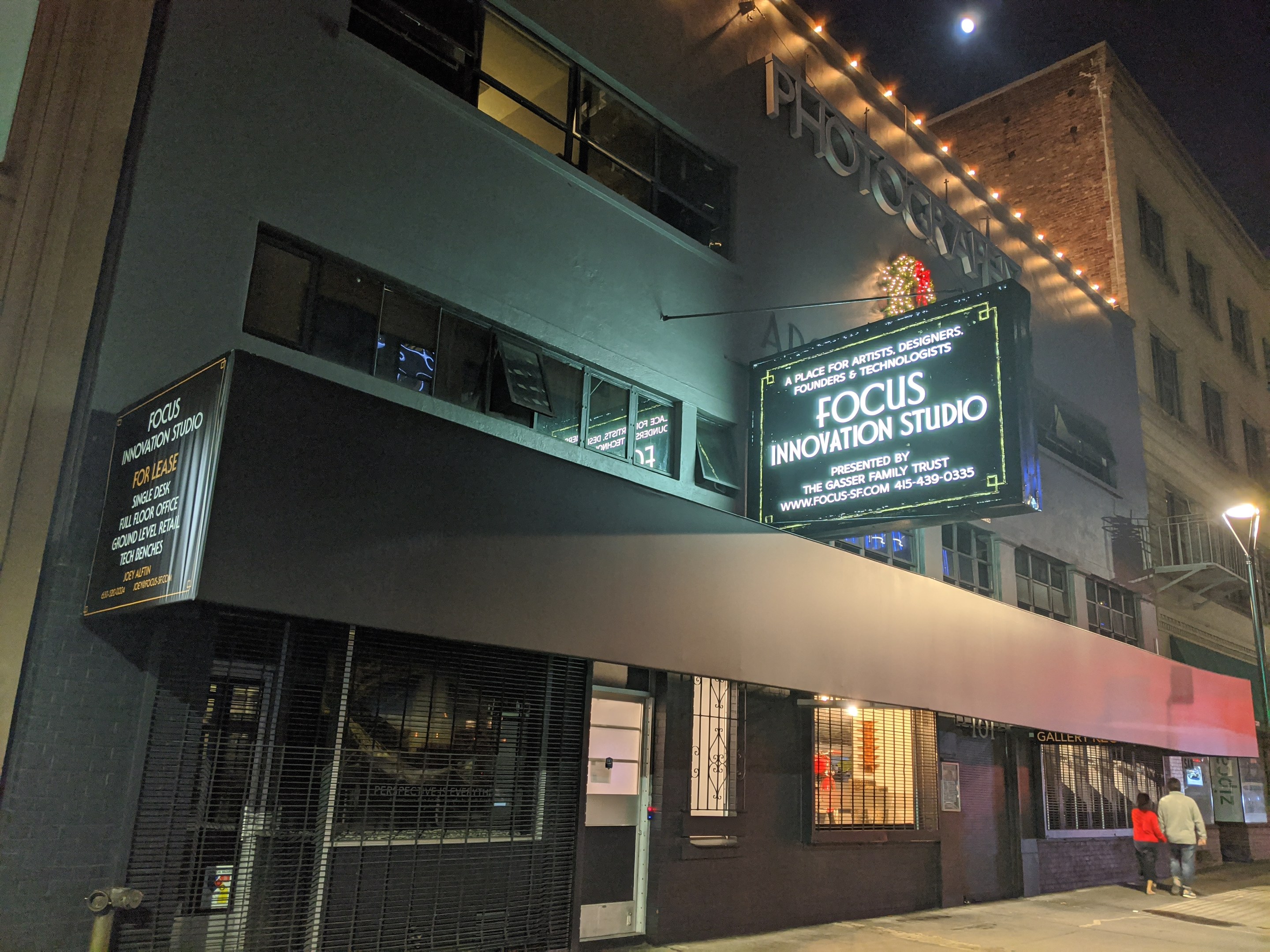 Das Focus Innovation Studio in New York City bei Nacht, mit beleuchteten Fenstern und Beschriftung, Menschen auf dem Gehweg und Gebäude im Hintergrund unter einem sichtbaren Nachthimmel.