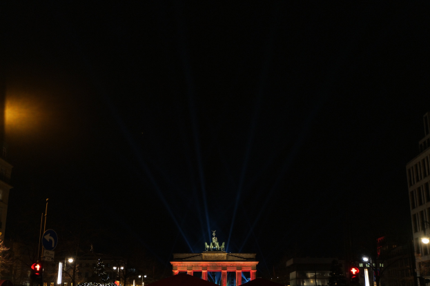 Brandenburger Tor nachts, von Straßenlaternen beleuchtet, umgeben von Gebäuden, Bäumen, Pfählen, Verkehrszeichen, Schildern und Zelten gegen einen dunklen Himmel.
