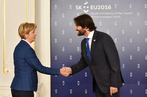 Bundeskanzlerin Angela Merkel und Bundespräsident Joachim Gauck geben sich die Hand vor einer Wand mit einem "EU-Gipfel"-Schild und einer Tür im Hintergrund, beide lächeln.