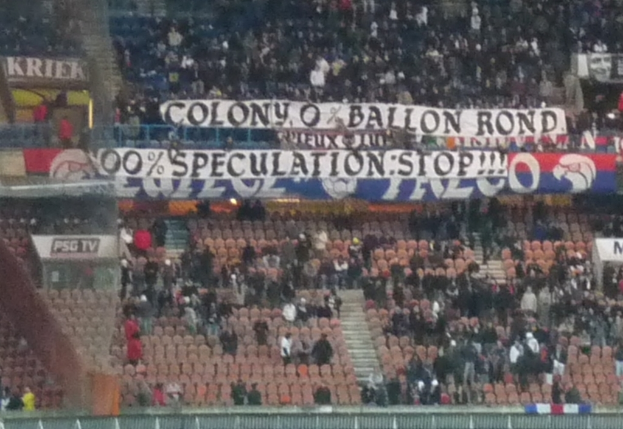 Ein volles Stadion mit Bannern und Stühlen im Vordergrund, einem Zaun unten und einer Treppe auf der linken Seite.