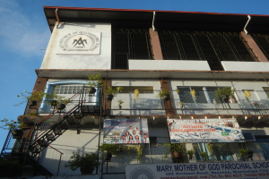 Maria Mutter Gottes Pfarrschule mit Fenstern, Geländern, Treppen, Topfpflanzen, Bannern und einem bewölkten Himmel im Hintergrund.