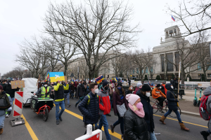 Eine große Gruppe von Menschen nimmt an einer Protestdemo auf einer Straße in Washington, D.C. teil, wobei sie Schilder und Banner schwenken und einige Fahrräder fahren, Schilder mit Stangen, Bäume und einen klaren blauen Himmel im Hintergrund.