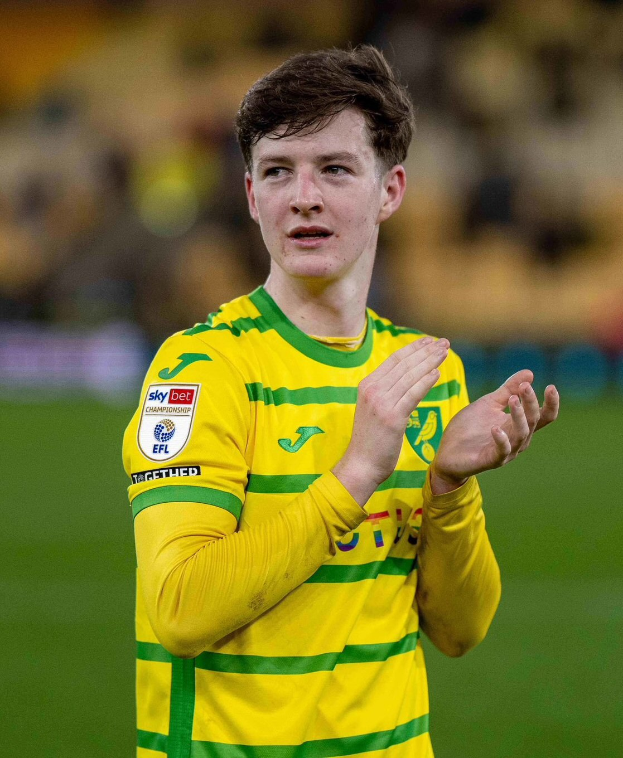 Ein junger Mann in einem gelb-grünen T-Shirt klatscht auf einem Fußballfeld, mit einem unscharfen Hintergrund.