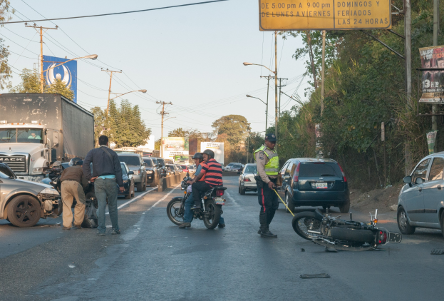 Gruppe von Menschen um ein verunglücktes Motorrad auf dem Seitenstreifen mit mehreren Fahrzeugen, darunter ein Lastwagen, im Hintergrund und Bäumen, Polen, Lichtern, Schildern und Himmel im Bild.