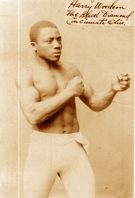 Ein Schwarz-Weiß-Foto eines Mannes im Boxring mit Handschuhen und Shorts, der entschlossen und konzentriert schaut.