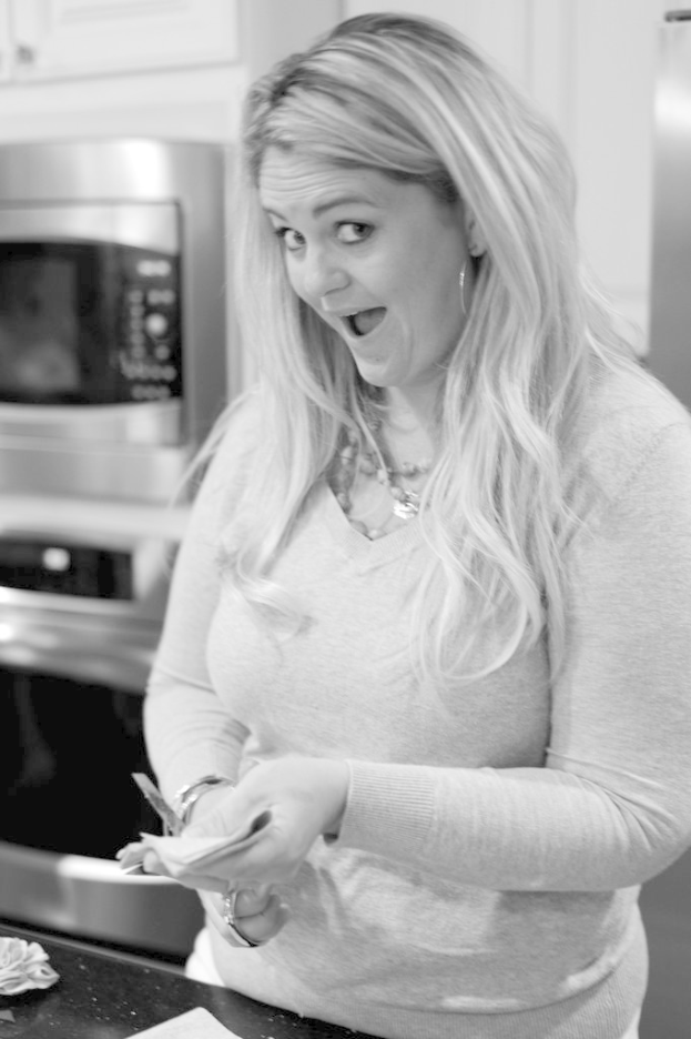 Eine Frau in einem T-Shirt steht mit einer Schere in der Hand, mit einem Ofen und einem weißen Schrank links von ihr.