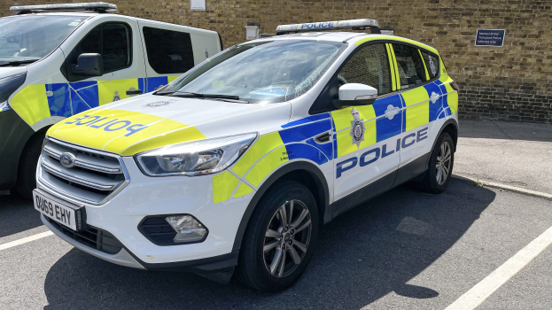 Zwei Polizeiautos nebeneinander auf einem Parkplatz mit einer Wandtafel im Hintergrund geparkt.