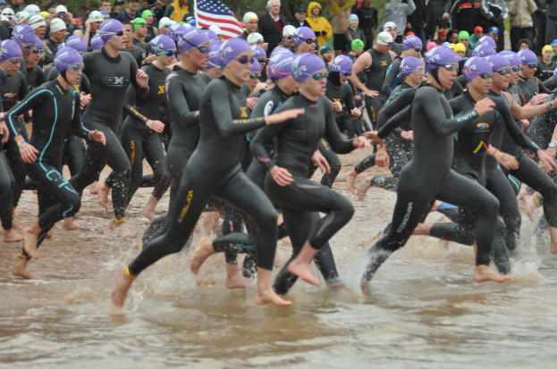 Menschen in Badesachen laufen durch flaches Wasser, mit anderen im Hintergrund und einer Fahne im Bild.