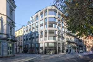 Ein großes modernes Bürogebäude mit vielen Fenstern, umgeben von Straßeninfrastruktur, Fahrzeugen, Fußgängern, Bäumen und einem bewölkten Himmel, das als neue Firmenzentrale dient.