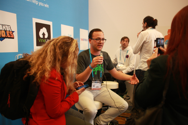 Ein Interview mit Menschen, die Mikrofone und eine Kamera halten, mit Personen im Vordergrund und einem Banner links, während der Hintergrund klar ist.