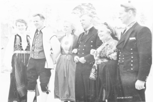 Eine Gruppe von Menschen in den 1930er Jahren, die in historischer Kleidung posieren, mit Bäumen im Hintergrund und der Aufschrift 'Bayerische Familie in den 1930er Jahren' am unteren Bildrand.