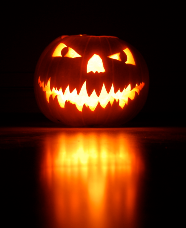 Ein geschnitzter Kürbis sitzt auf dem Boden mit einem dunklen Hintergrund.