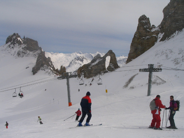 Menschen in Pullovern skifahren auf dem Eis mit einer Seilbahn, Bergen und einem bewölkten Himmel im Hintergrund.