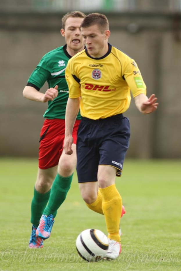 Zwei Männer beim Fußballspiel auf einem grünen Feld mit einem Ball, mit unscharfem Hintergrund und Text unten.