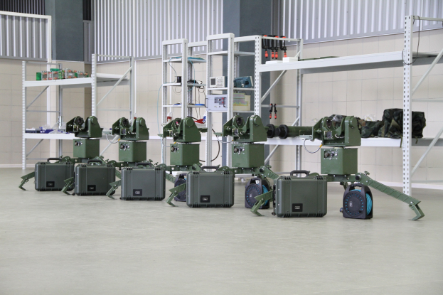 Militärroboter auf einem Boden sitzend mit Koffern und Gegenständen auf Gestellen, in der Nähe einer Wand und eines Geländers als Teil eines Verteidigungs-systems positioniert.