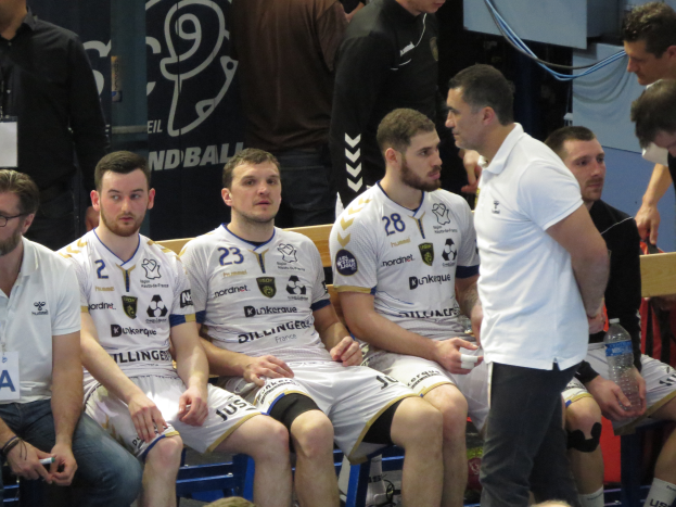 Eine Gruppe von Männern sitzt auf einer Bank, einige halten Flaschen, mit einem Banner im Hintergrund mit der Aufschrift "Nordkraque vs Bordeaux."