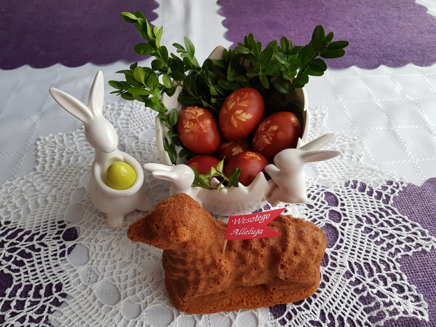 Ein Tisch mit einer Decke darauf h├Ąlt eine Sch├Âssel mit bunten Ostereiern und Osterhasenfiguren darauf.