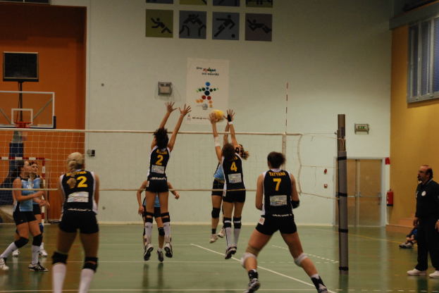 Ein Volleyballspiel auf einem Indoor-Court mit einem Basketballkorb im Hintergrund.