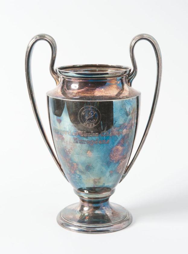 Der UEFA-Champions-League-Pokal, eine silberne und blaue Stahlschale mit zwei Griffen, die mit "UEFA Champions League" beschriftet ist, vor einem weißen Hintergrund dargestellt.