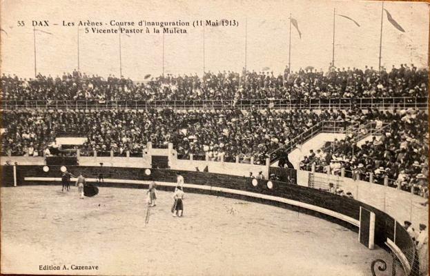 Schwarzes und weißes Foto eines Boxkampfes in einem Stadion mit Zuschauern auf den Tribünen und einer Gruppe von Menschen in der Mitte.