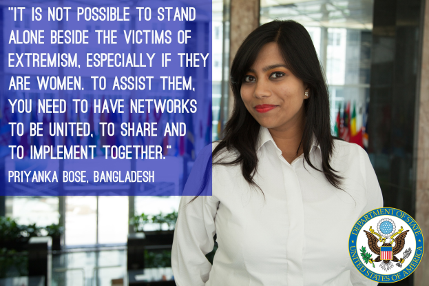 Eine Frau in einem weißen Hemd steht vor einem Gebäude mit einem Zitat über die Unterstützung von Opfern des Extremismus, mit einem Logo in der rechten unteren Ecke.