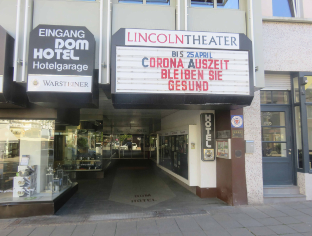 Das Lincoln Theater in Berlin, Deutschland, mit Glasfenstern und -türen und einer Texttafel draußen sowie einer belebten Stadtkulisse drinnen.