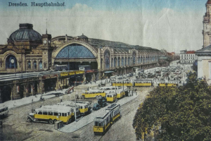 Ein altes Postkartensuvenir zeigt einen belebten Dresdner Bahnhof mit Fahrzeugen, Menschen, Bäumen, Gebäuden und einem bewölkten Himmel, mit der Aufschrift "Dresden Hauptbahnhof" oben.
