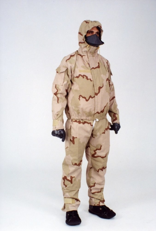 Eine Person in einem camouflagegemusterten Schutzoverall mit Kapuze und Vollgesichtsschutz steht vor einem weißen Hintergrund.
