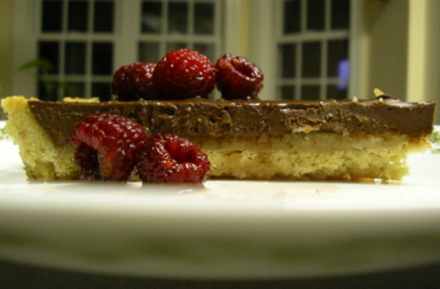 Ein Schokoladengebäck mit Kirschen auf einem weißen Teller, vor einem weißen Glasfenster.