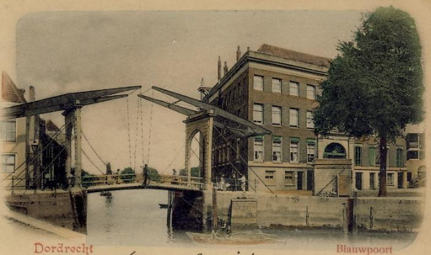 Altes Schwarz-Weiß-Foto einer Brücke, die einen Fluss überspannt, mit Gebäuden, Bäumen und einem klaren Himmel im Hintergrund und verstreuten Baumaschinen und Materialien unten.
