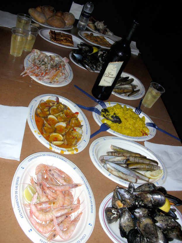 Ein Tisch mit Tellern voller Garnelen, Schalen und verschiedenen Speisen, begleitet von Taschentüchern, Flaschen und Gläsern.