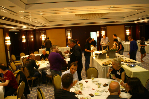 Ein Restaurant-Innenraum mit Tischen und Stühlen, Gruppen von Menschen, die essen, und einem zentralen Tisch mit verschiedenen Speisen, einige Menschen stehen und essen.