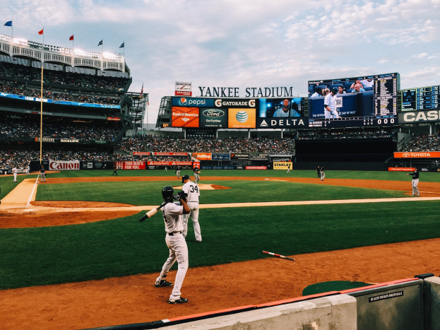 Baseballspiel im Yankee Stadium mit Spielern auf dem Feld und Zuschauern in den Rängen bei bewölktem Himmel.
