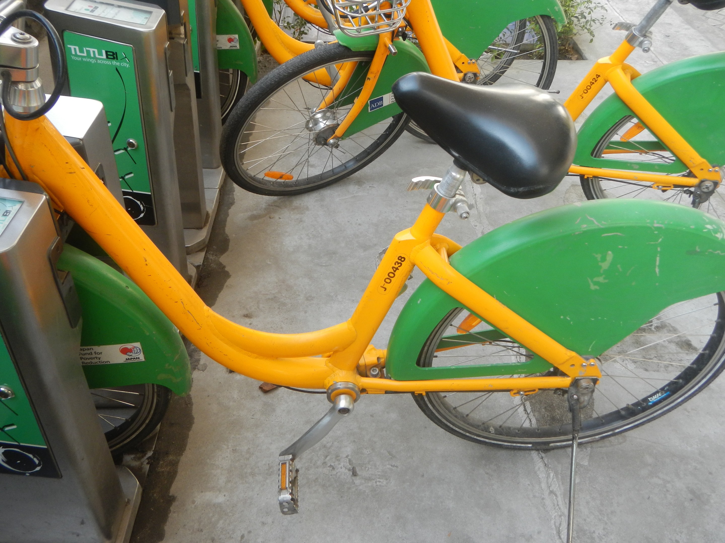 Eine Reihe gelber und grüner Fahrräder nebeneinander geparkt mit Maschinen links und Pflanzen im Hintergrund.