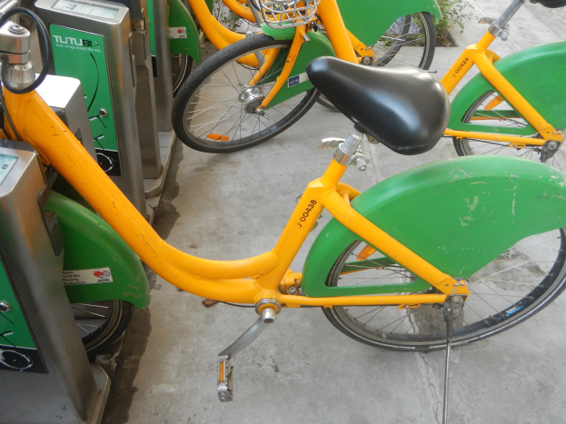 Eine Reihe gelber und grüner Fahrräder nebeneinander geparkt mit Maschinen links und Pflanzen im Hintergrund.