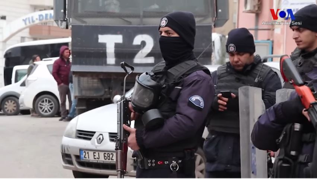 Eine Gruppe von Polizisten in Uniformen mit Waffen in der Hand steht auf einer Straße in Ankara, Türkei, während einer Anti-Regierungsdemo, mit Fahrzeugen, Menschen, Gebäuden und Texttafeln im Hintergrund.