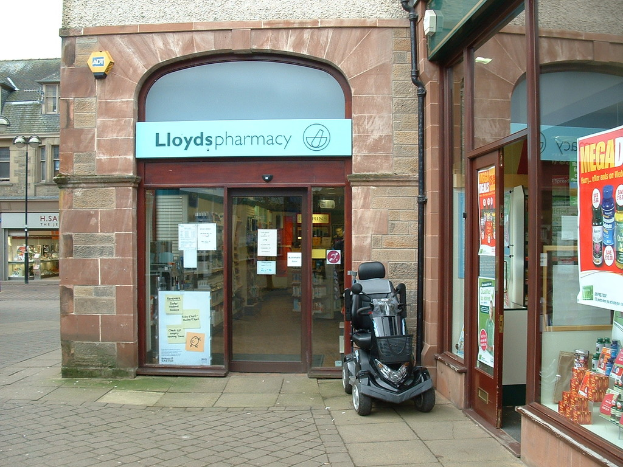 Ein Apothekenladen mit einem Fahrzeug davor und einem Gebäude links daneben.