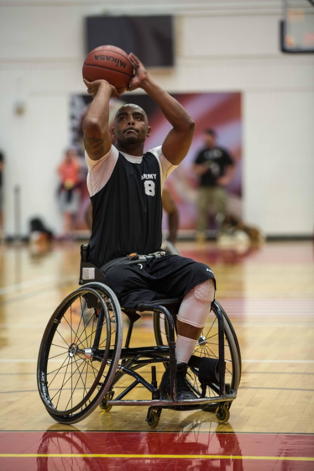 Ein Mann sitzt im Rollstuhl und hält einen Ball in der Hand, mit ein paar Menschen im Hintergrund.