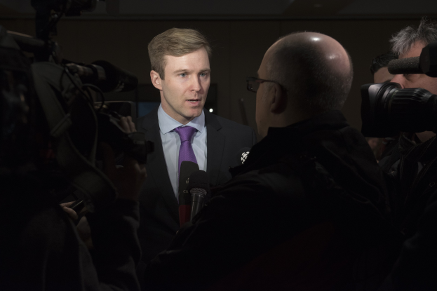 Ein Mann im Anzug mit Brille spricht in ein Mikrofon, während zwei Kameramänner ihn während eines Interviews aufnehmen.