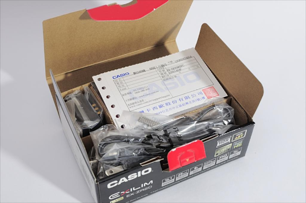 Eine offene Casio-Schachtel auf einer weißen Oberfläche, die interne Drähte und einen Beleg zeigt.