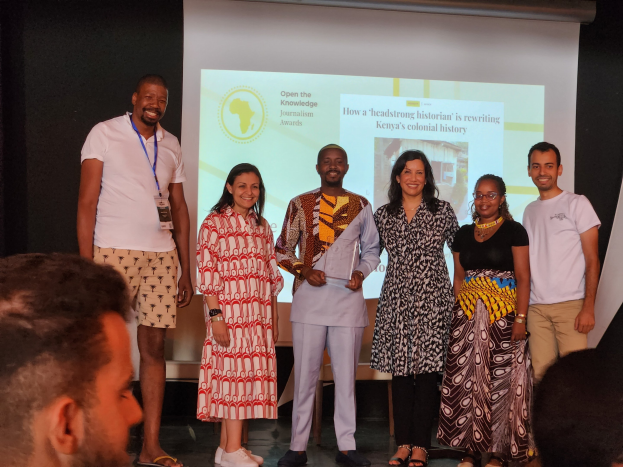 Eine Gruppe von Menschen auf einer Bühne, die lächeln und posieren, mit sitzenden Zuschauern unten und einem Bildschirm im Hintergrund, der 'Open the Knowledge Journalism Awards 2019' anzeigt.