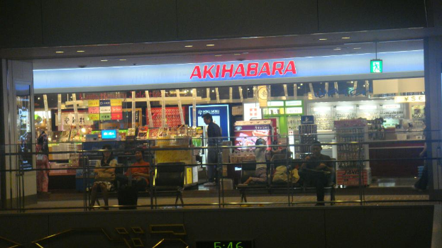 Ein Geschäft mit zwei Bänken davor, auf denen jeweils einige Menschen sitzen, einem Schild darüber und einer Wand mit einem Zaun unten.