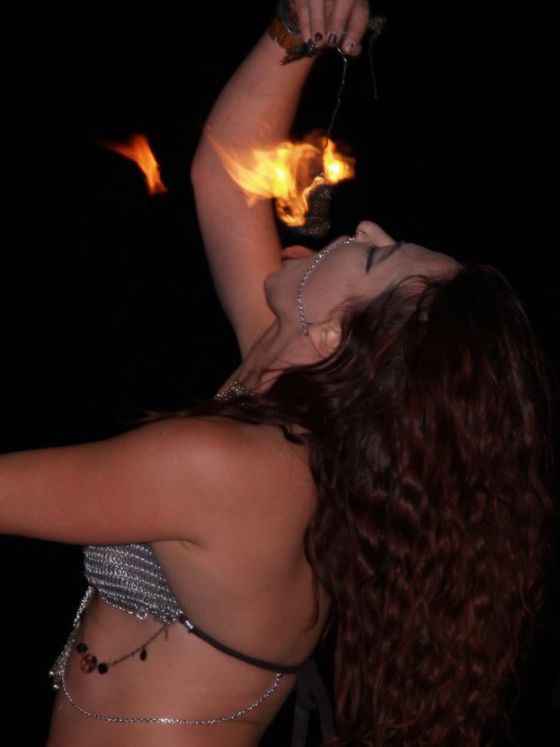 Frau steht über einem Ort und versucht, ein brennendes Objekt in ihrer Hand zu essen.