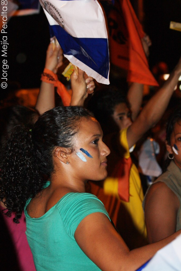 Frauen in grünen T-Shirts bei einer Demonstration, die weiße Zettel in den Händen halten, mit vielen anderen Mädchen hinter ihnen.
