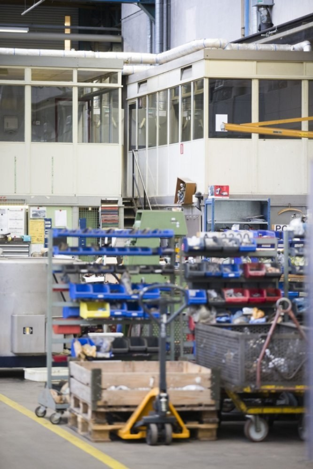 Ein großes Lager mit verschiedenen Geräten wie Wagen, Schränken und einer Kiste, mit einer Glaswand und Rohren im Hintergrund.