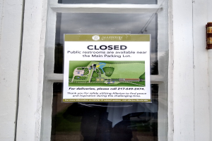 Gläserne Tür mit einem Schild, auf dem "Geschlossene öffentliche Toiletten in der Nähe des Hauptparkplatzes" steht, und einem unklaren Objekt auf der rechten Seite.